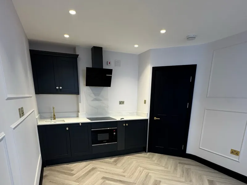 Finished kitchen in a renovated Mayfair flat with dark units, white walls and a herringbone floor