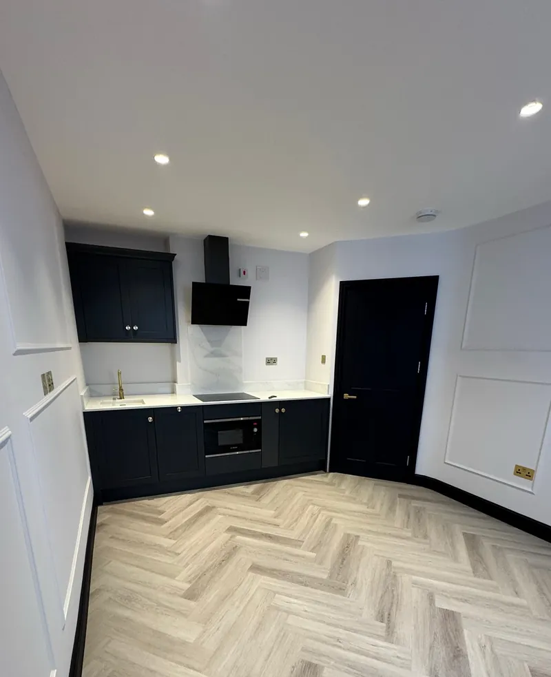 Finished kitchen in a renovated Mayfair flat with dark units, white walls and a herringbone floor